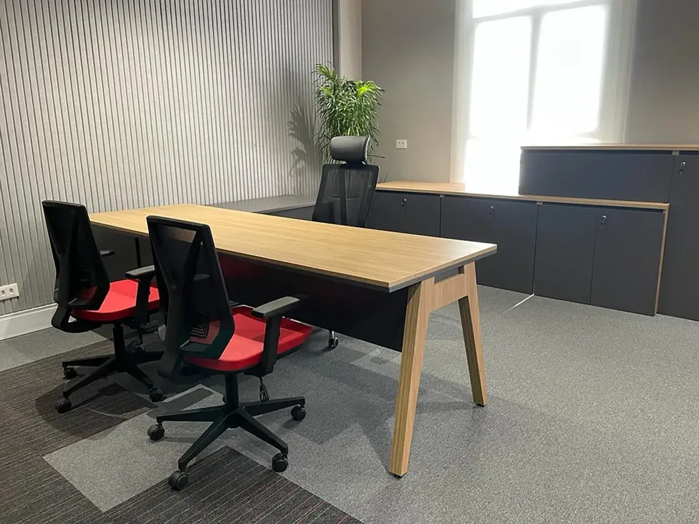 Escritório com mesa de trabalho, cadeiras vermelhas e painel acústico