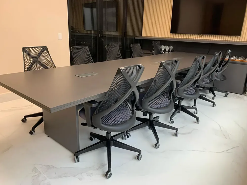 Sala de reunião com mesa grande, cadeiras e televisão na parede